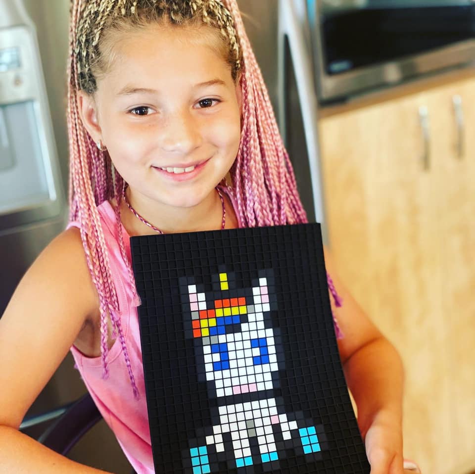 Petite fille souriante montrant sa licorne en pixel art terminée sur une grille Dodocraft