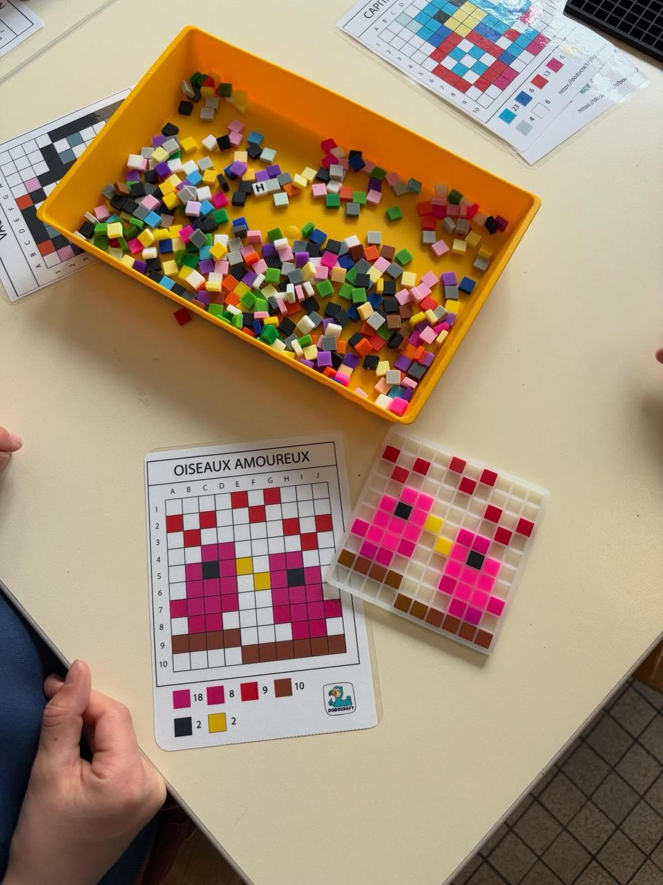Atelier pixel art en classe : bac de pixels en silicone, carte modèle Oiseaux amoureux et grille en cours de réalisation