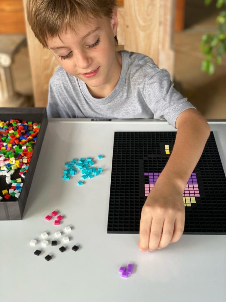 Enfant concentré en train de placer des pixels sur sa grille Dodocraft à la maison