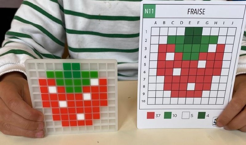 Enfant tenant sa grille de pixel art fraise terminée à côté de la carte modèle Dodocraft